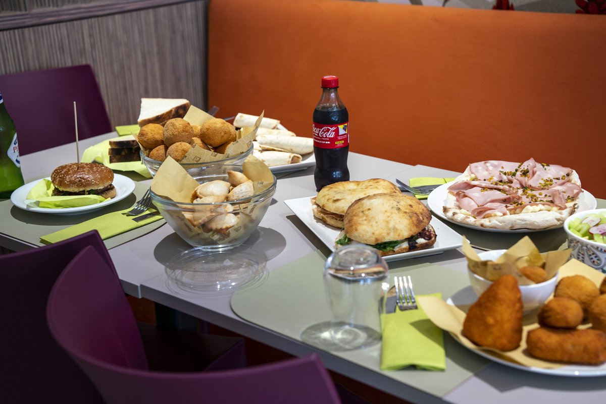 Arancini, pucce, pizza con mortadella e pistacchio, crocchette e Coca-Cola sul tavolo de La Bussola dei Sapori